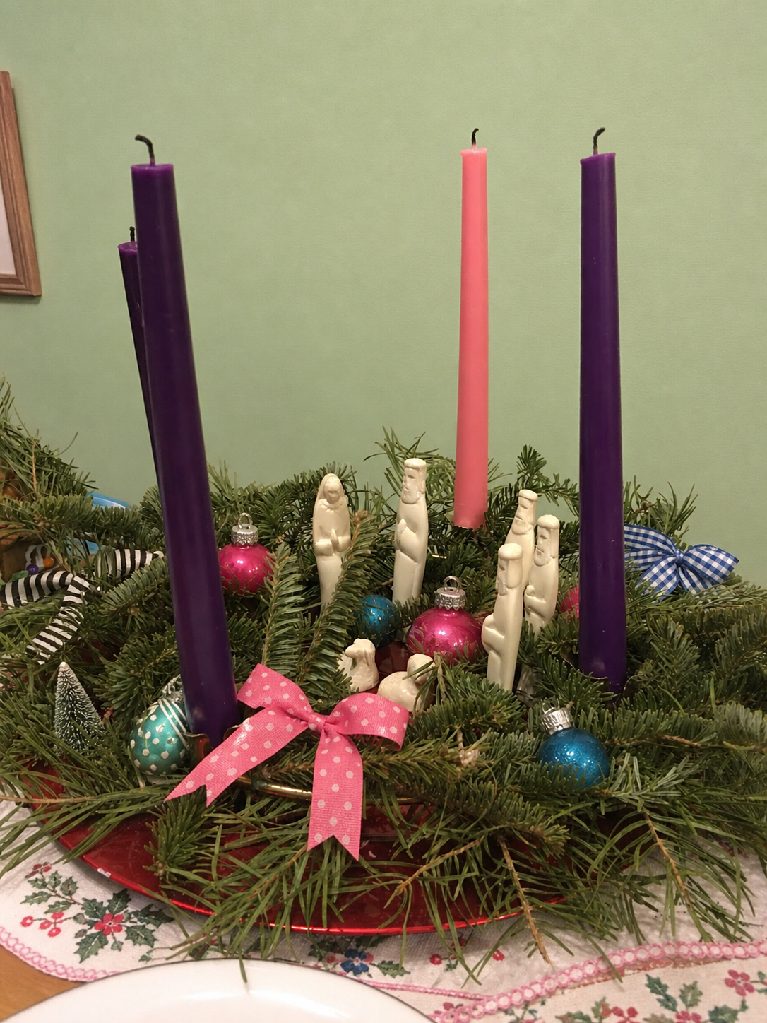 Advent wreath with three purple candles, one rose candle, mint wall, colorful ornaments, and black-and-white ribbon