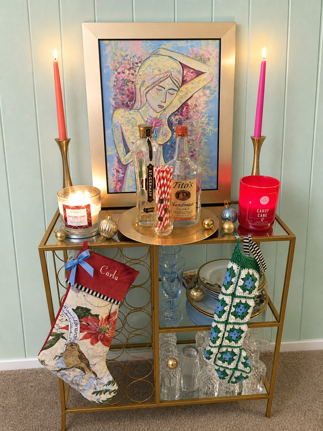 Gold Christmas bar cart with coral and hot pink candles, colorful glassware, stockings, and a mint wall