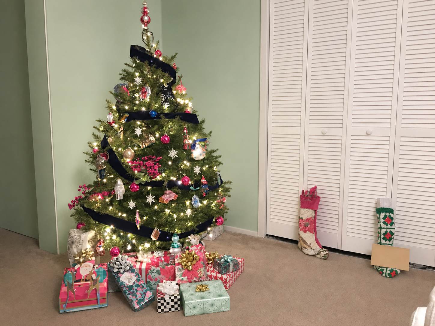 Christmas tree and gifts in coral, pink, mint, cornflower, black, white, and gold against a mint wall