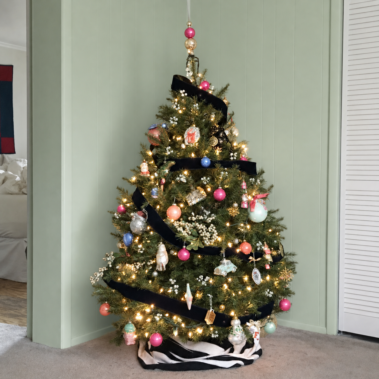 Christmas tree with black ribbon, hot pink, coral, cornflower, mint, white, and gold ornaments against a mint wall